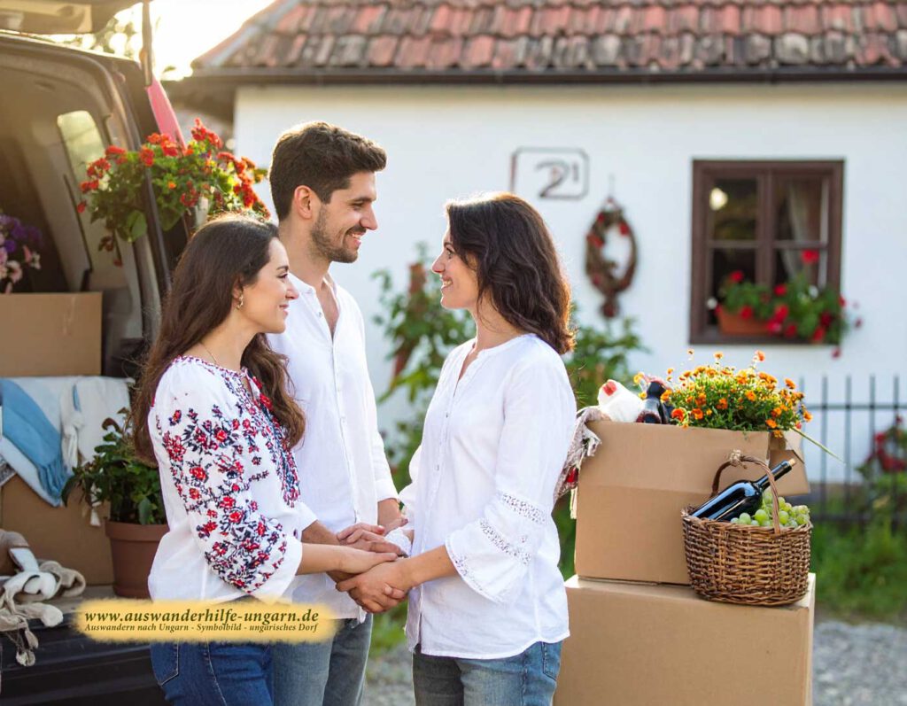 Drei lachende Menschen mit schönen Haaren halten sich vor einem weiß getünchten Dorfhaus (Nr. 21) an den Händen; offener Umzugswagen, Umzugskartons, Weidenkorb, Blumen und bestickte Blusen – herzliches Ankommen in Ungarn.