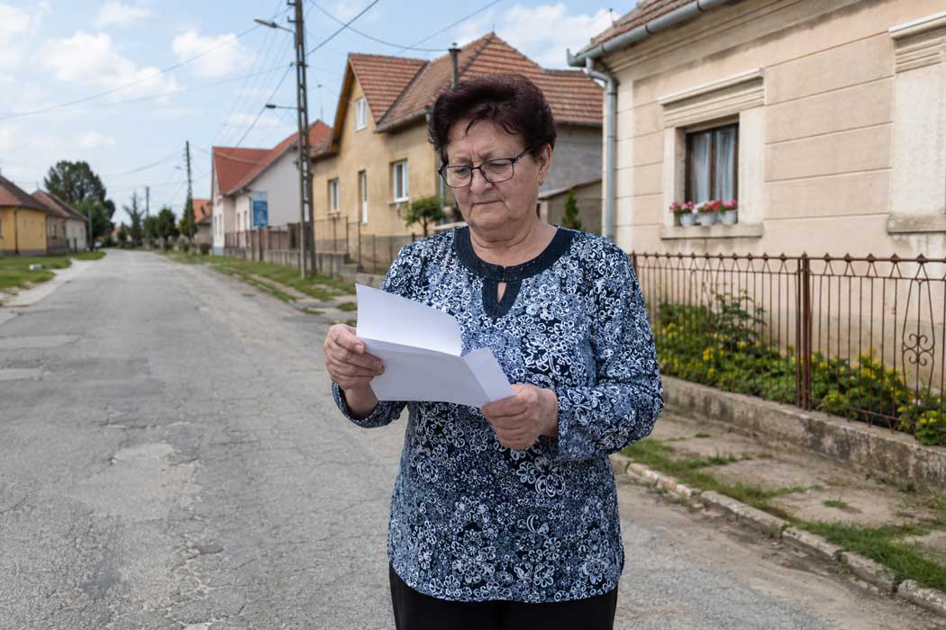 Auswandern nach Ungarn - Rentnerin liest Behördenbrief auf einer Dorfstraße im Komitat Zala mit ungarischen Häusern und Stromkabeln