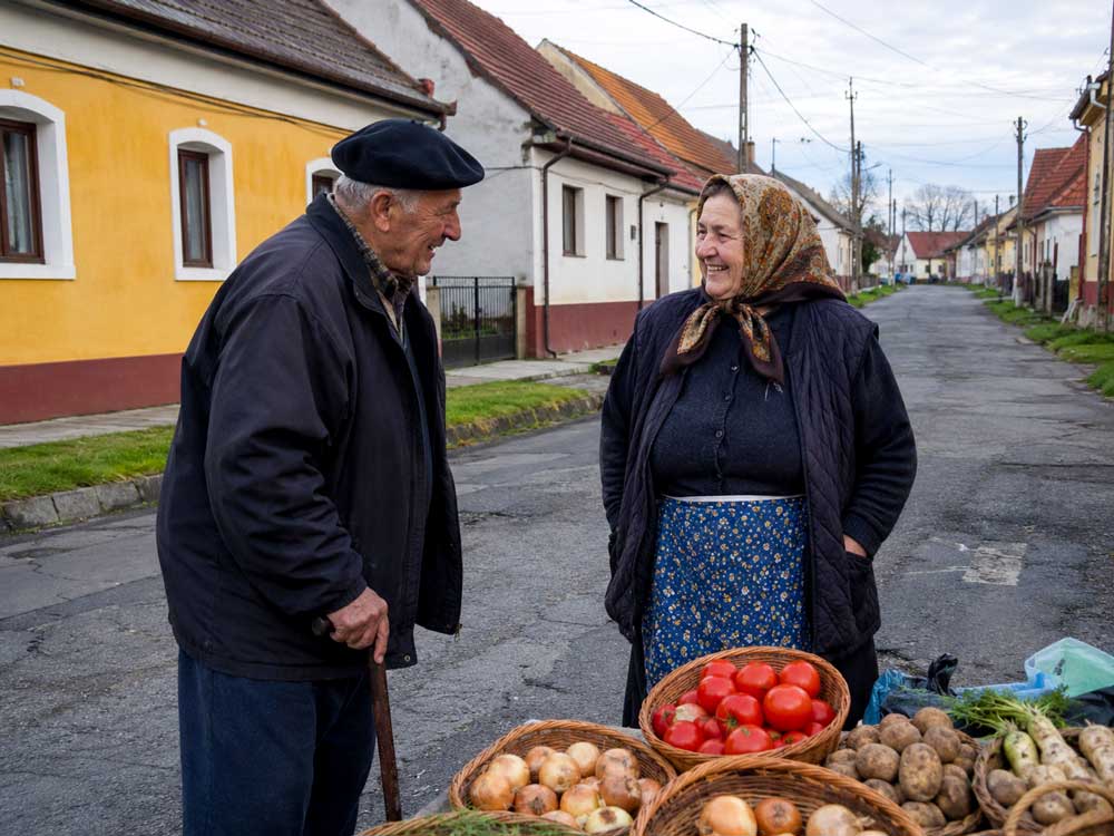 Zwei ältere Menschen unterhalten sich an einem kleinen Straßenverkauf mit Gemüse in einer ungarischen Ortschaft. Das Bild zeigt Auswandern nach Ungarn im Komitat Bacs Kiskun mit authentischem Dorfleben und Begegnung.