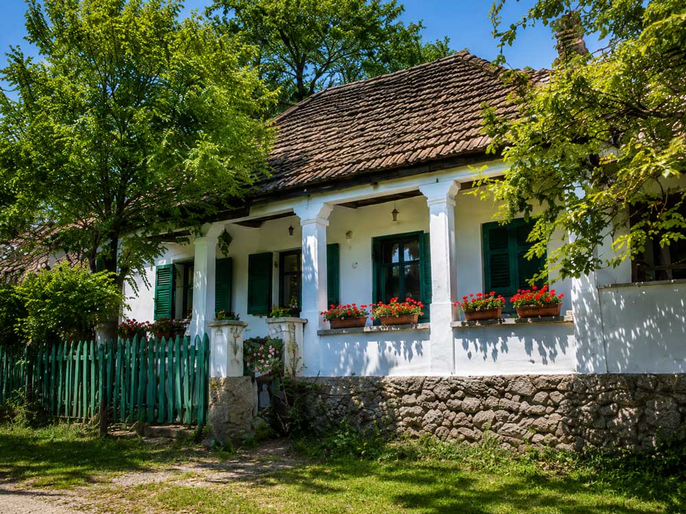 Auswandern nach Ungarn im Komitat Baranya: weißes Landhaus mit grünen Fensterläden, Blumen, Veranda und altem Ziegeldach.