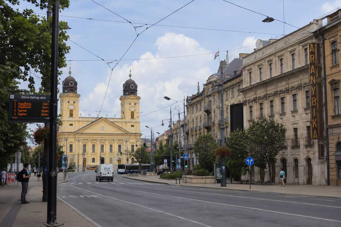 Auswandern nach Ungarn in Debrecen mit breiter Stadtstraße, Straßenbahndrähten, historischer Kirche, ungarischer Beschilderung und ostungarischem Stadtgefühl.